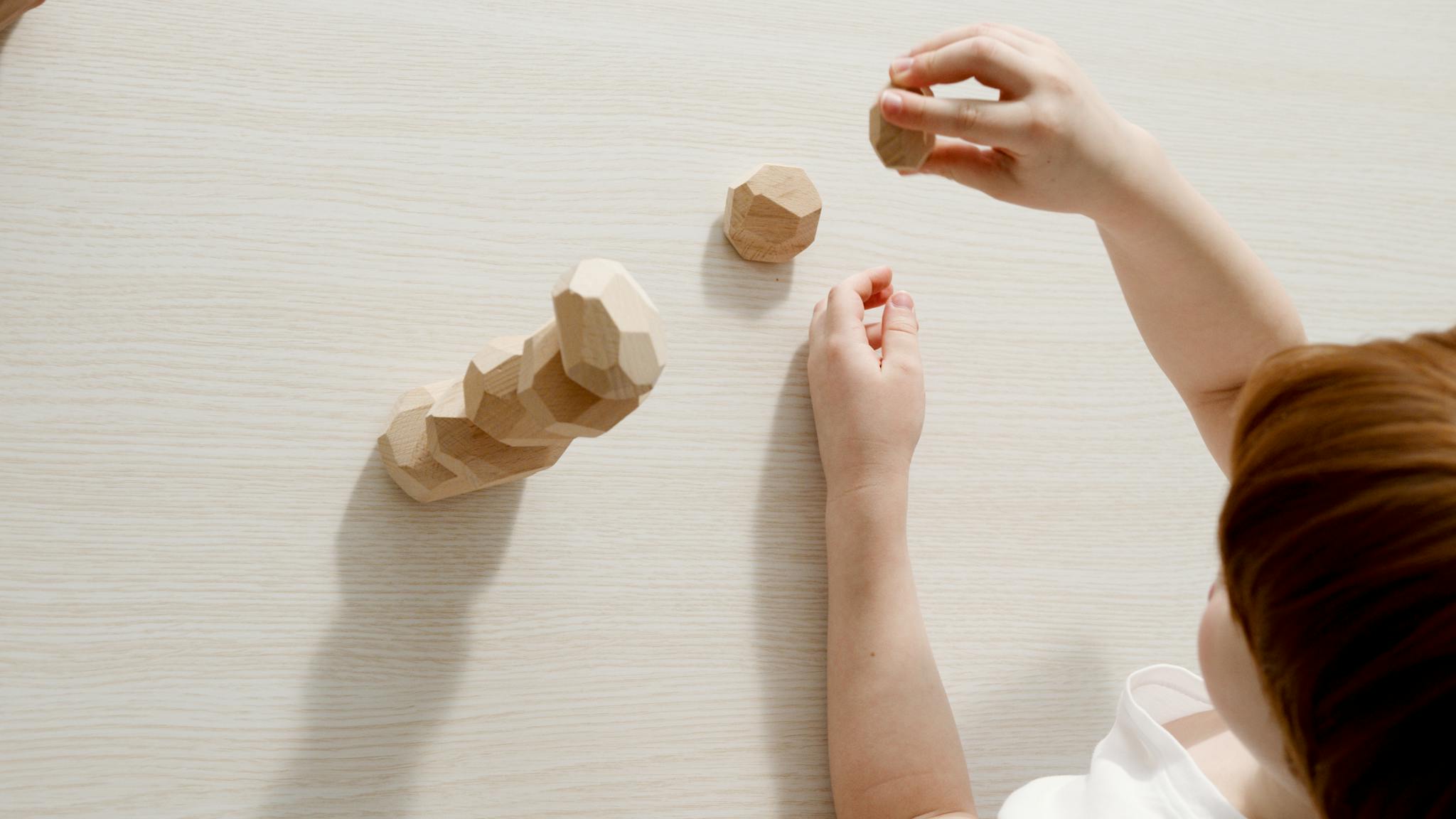 A child engaging with natural wooden stacking toys on a light table, developing fine motor skills.