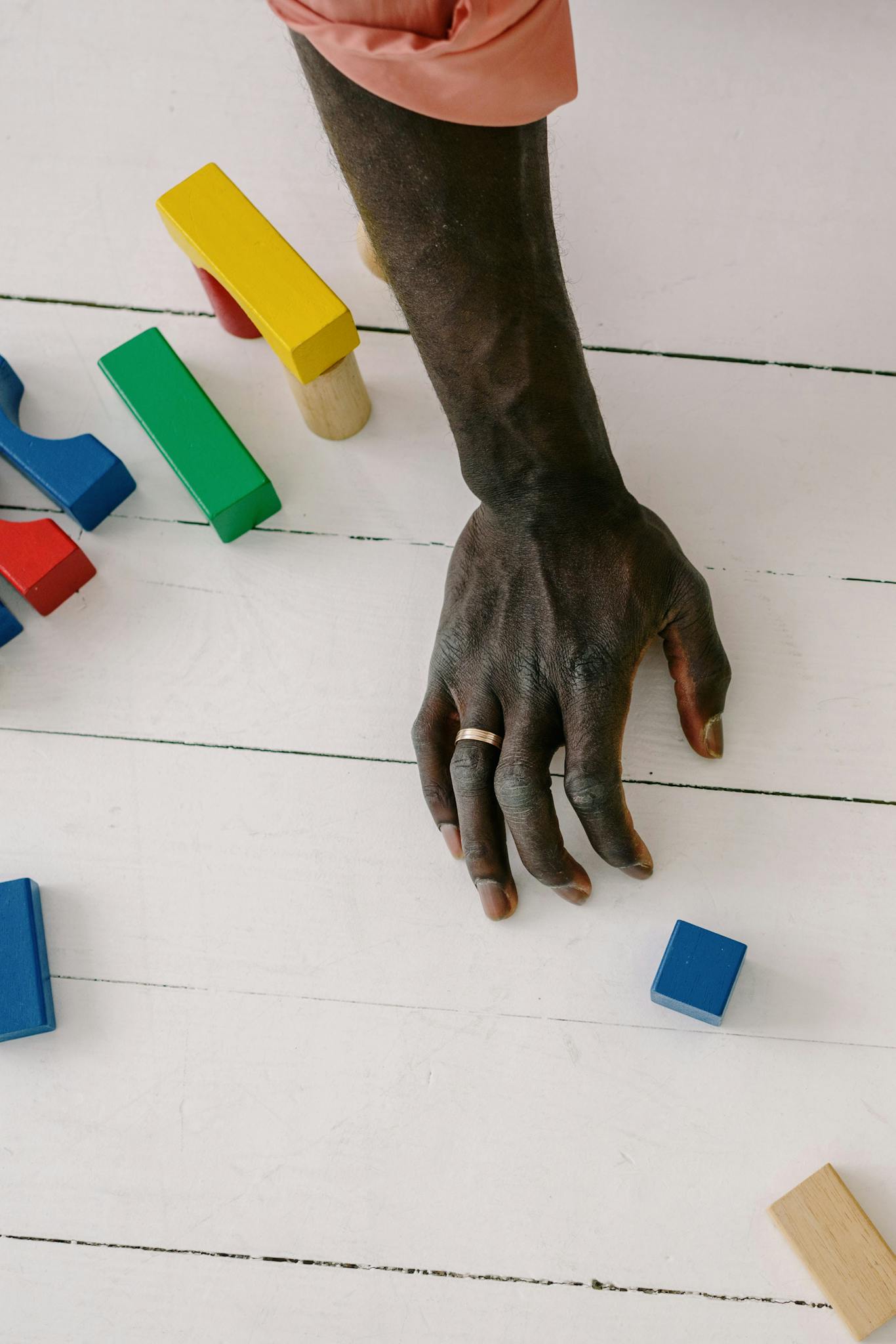 Close-up of a child's hand playing with colorful wooden blocks on a white surface.