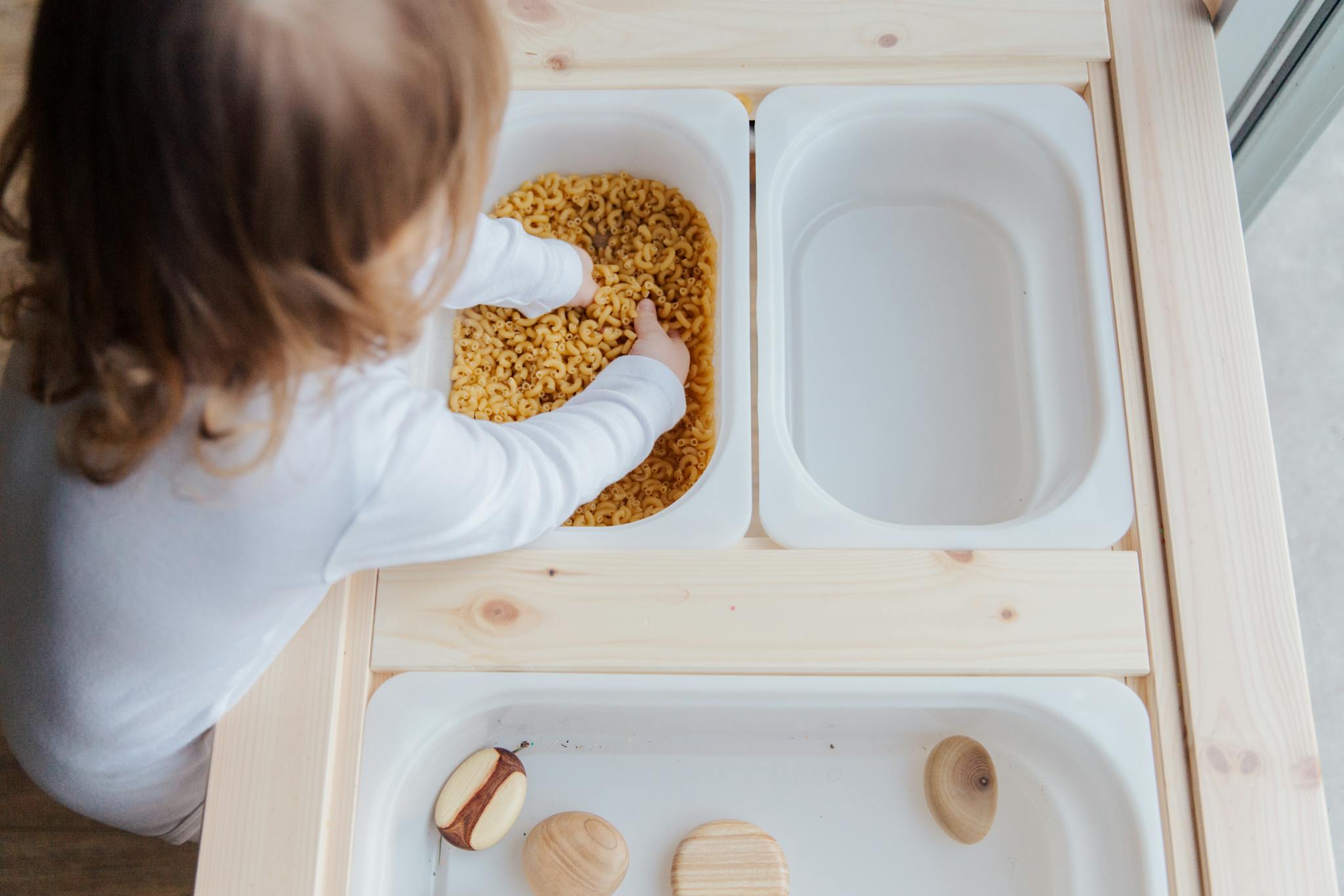 Curious child engaging in sensory play with pasta, exploring textures indoors.